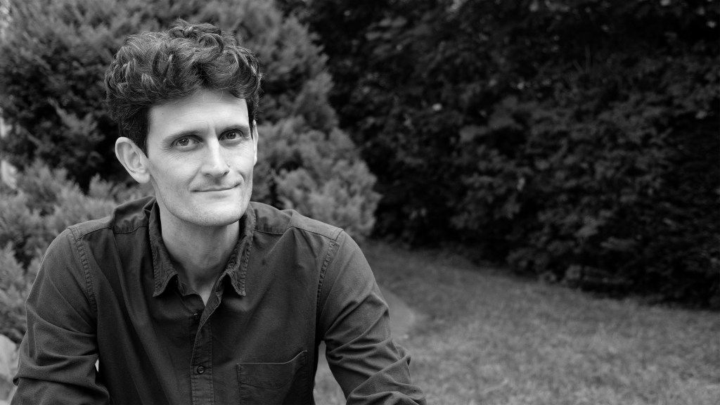 A black and white photo of Philip, sitting outside with a garden in the background.